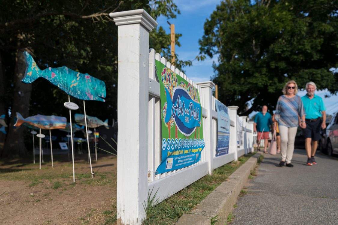 People walk down Chatham's Main Street in front of the annual Art in the Park display. 